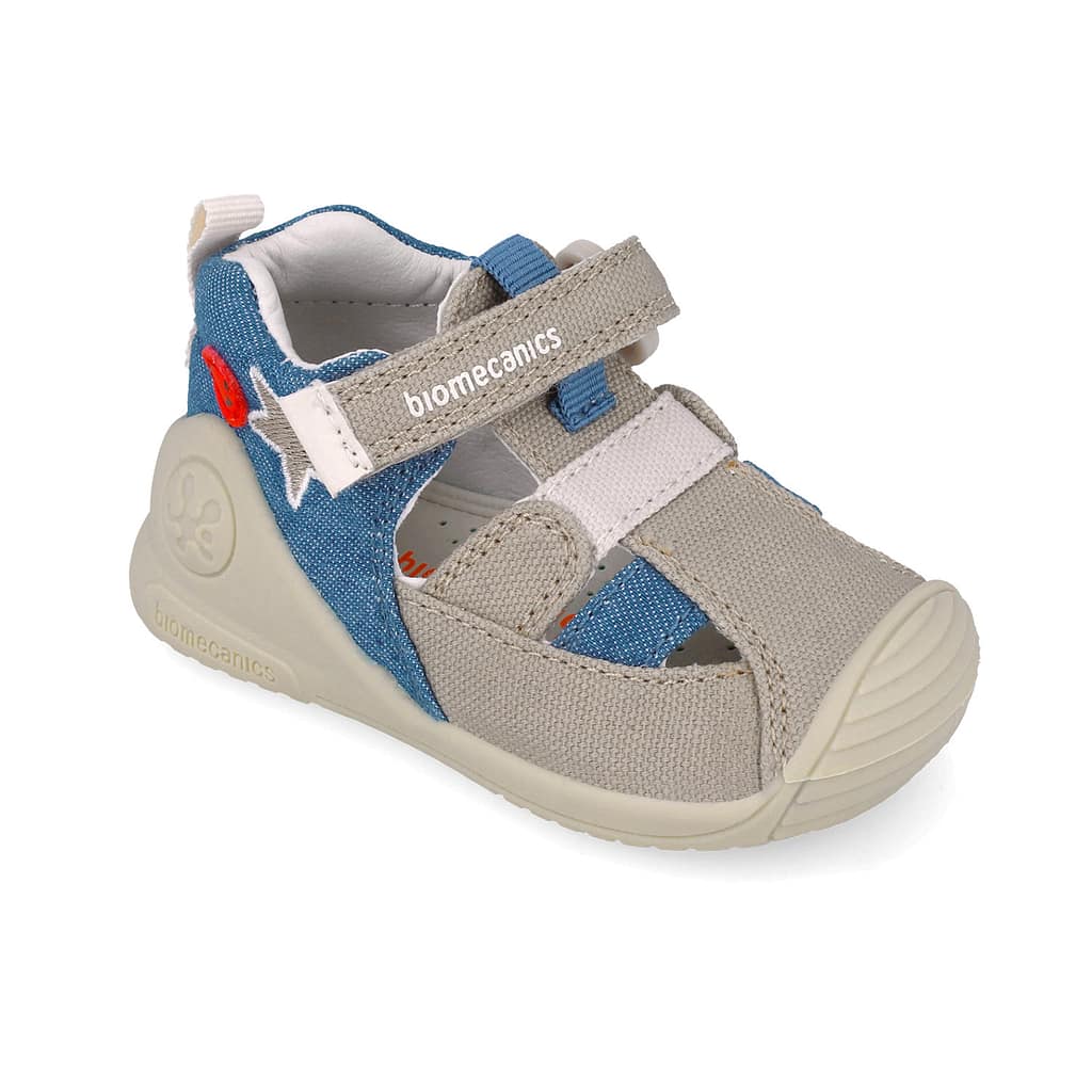 Toddler athletic shoe with blue denim and beige straps, Velcro closure, exposed stitching and beige sole; brand 'biomecanics' visible on strap edge.